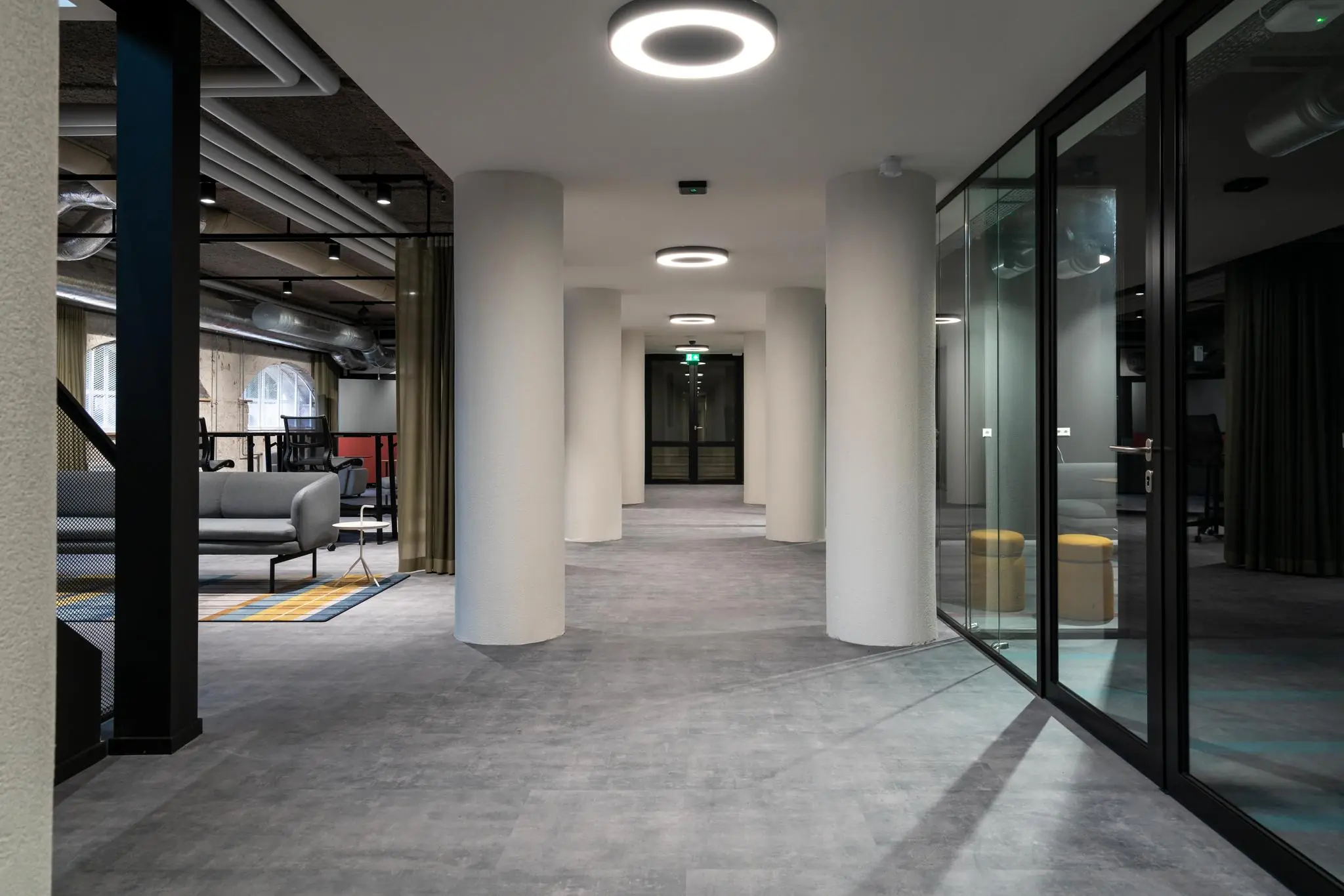 Moderne kantoorgang aan de Wassenaarseweg met glazen wanden, ronde pilaren en een minimalistisch interieur.