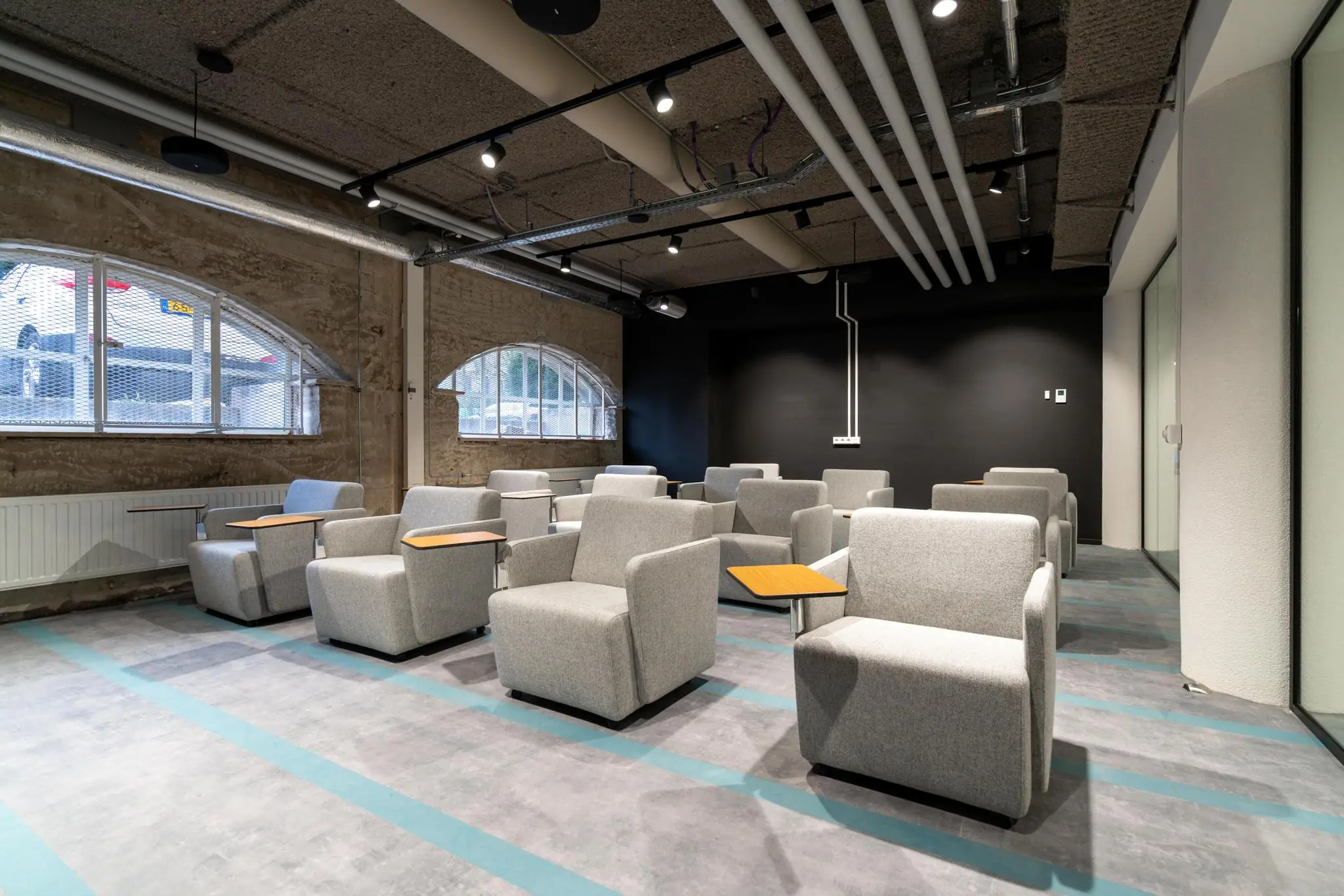 Moderne vergaderruimte aan de Wassenaarseweg met grijze loungefauteuils en kleine houten schrijftafels.