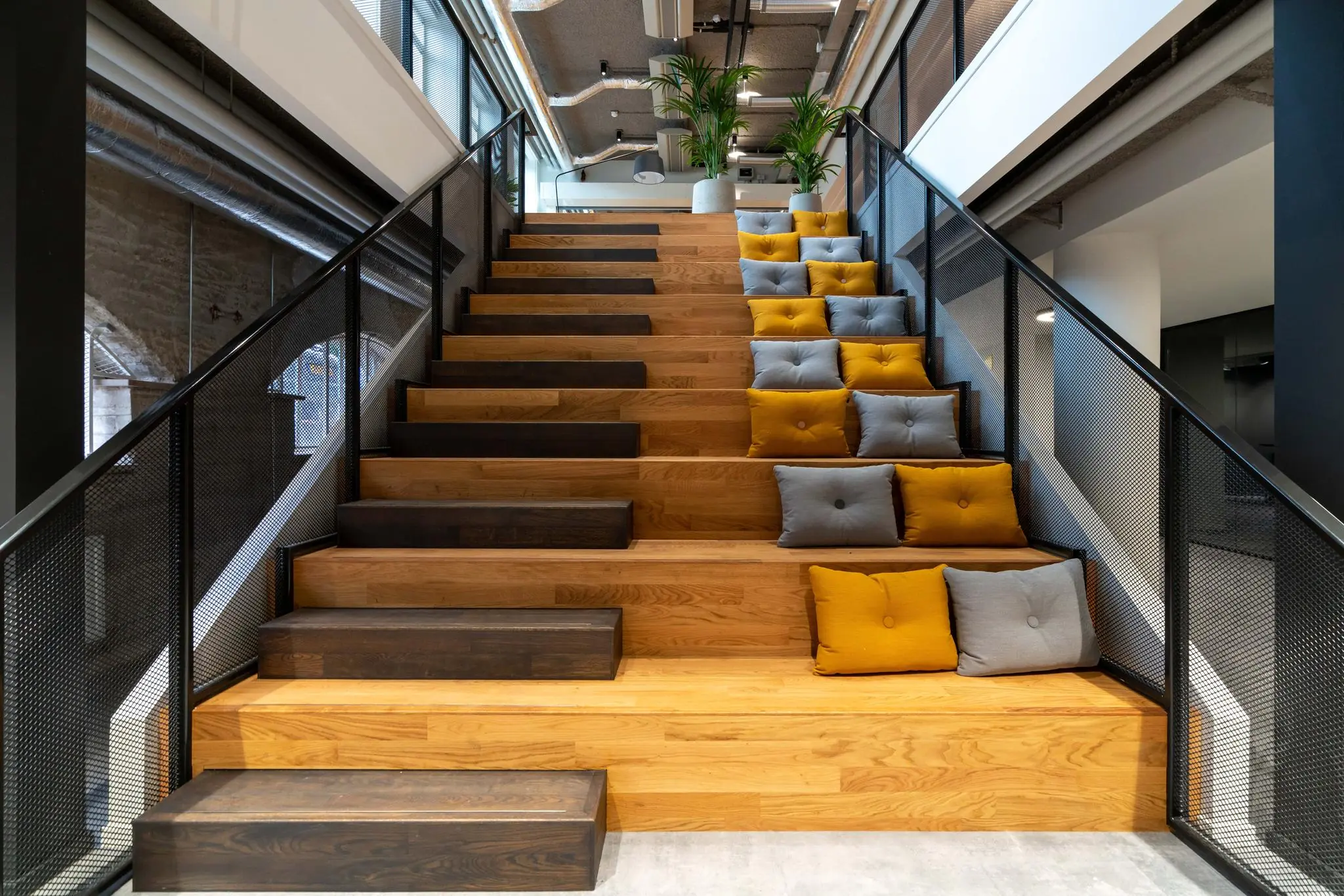Houten tribune-trap met grijze en okergele kussens in een modern kantoorpand aan de Wassenaarseweg.