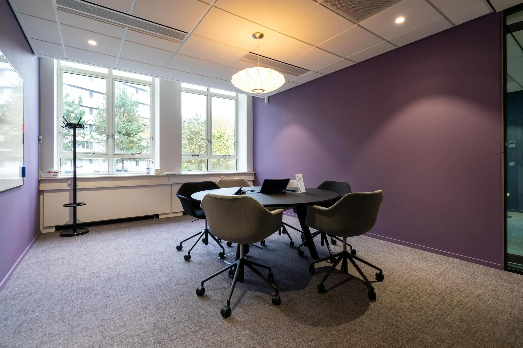 Moderne vergaderruimte aan de Wassenaarseweg met paarse muur, ronde tafel en vijf stoelen.