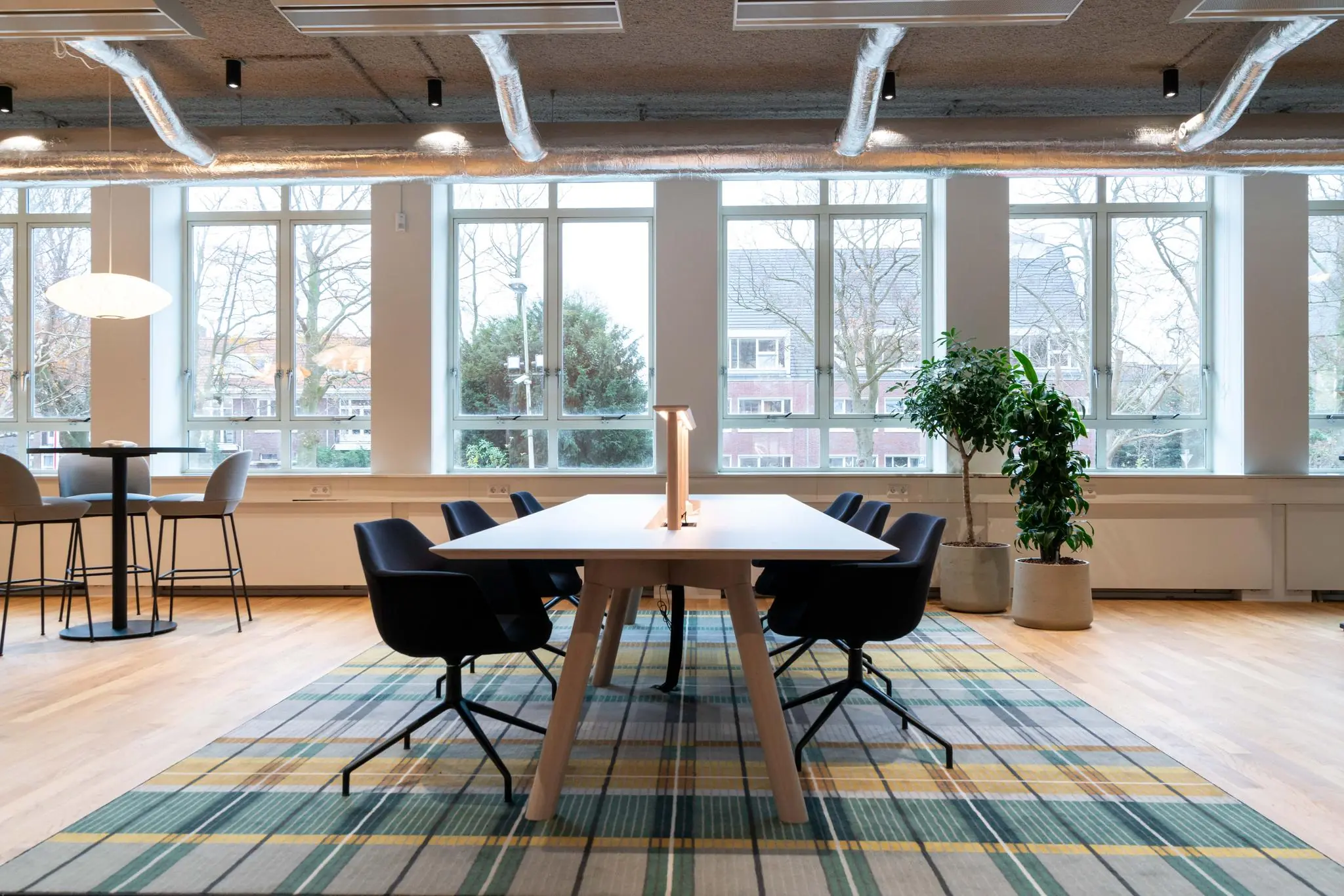 Moderne vergaderruimte aan de Wassenaarseweg met grote ramen, een lange tafel, zwarte stoelen en groene kamerplanten.