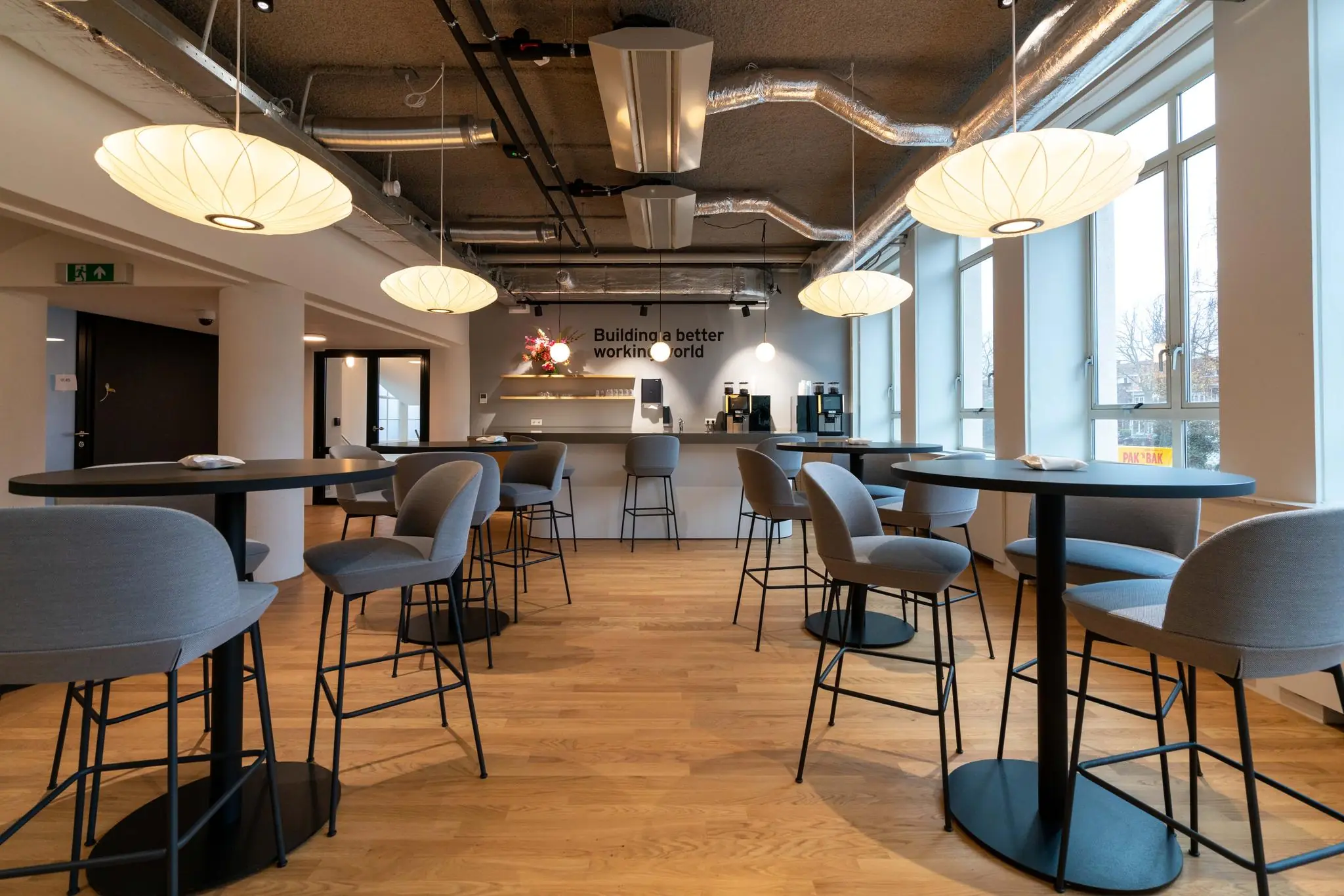 Moderne kantoorkantine aan de Wassenaarseweg met hoge tafels, grijze barkrukken en sfeervolle verlichting.