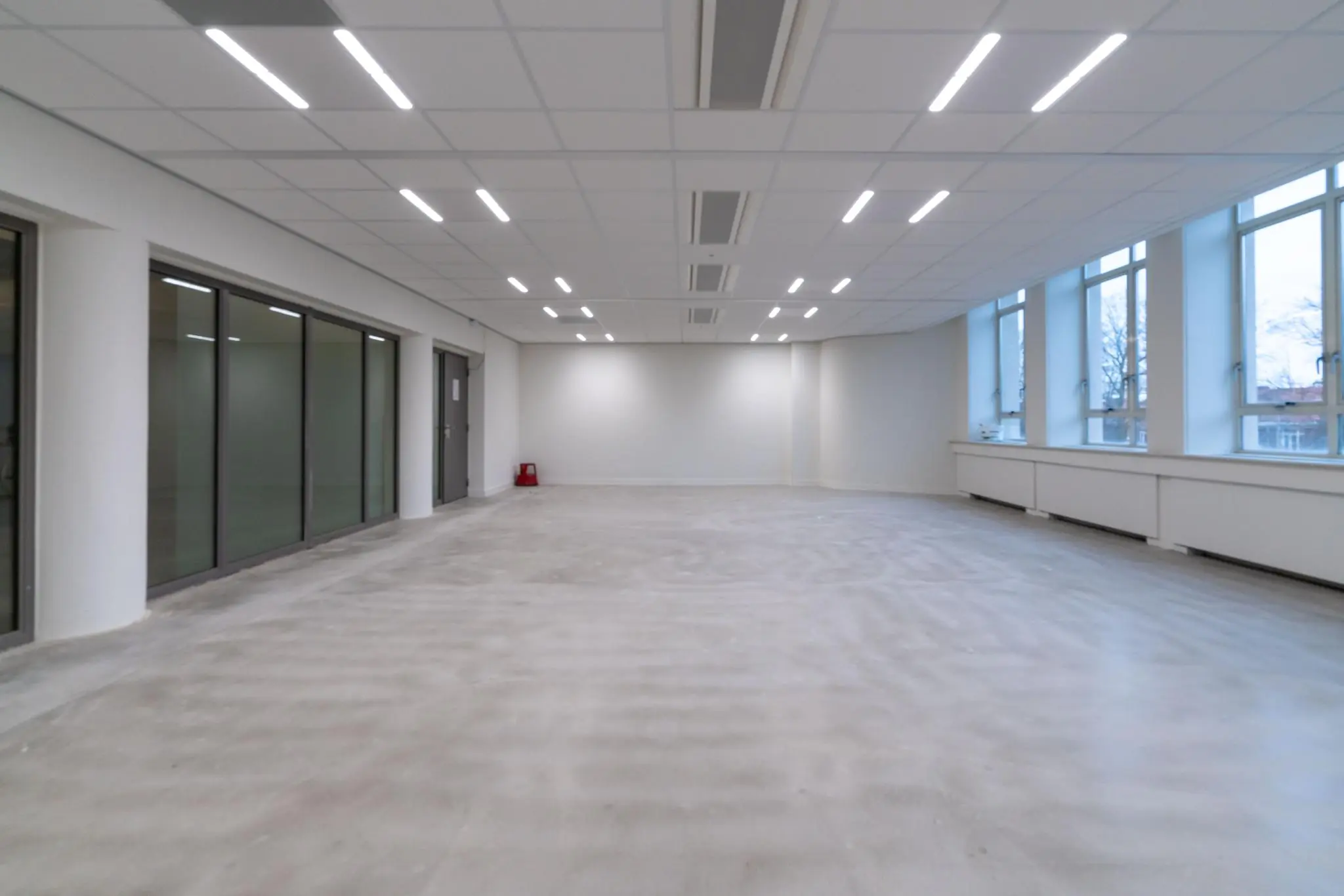 Lichte, lege kantoorruimte aan de Wassenaarseweg met grote ramen en een systeemplafond met ledverlichting.