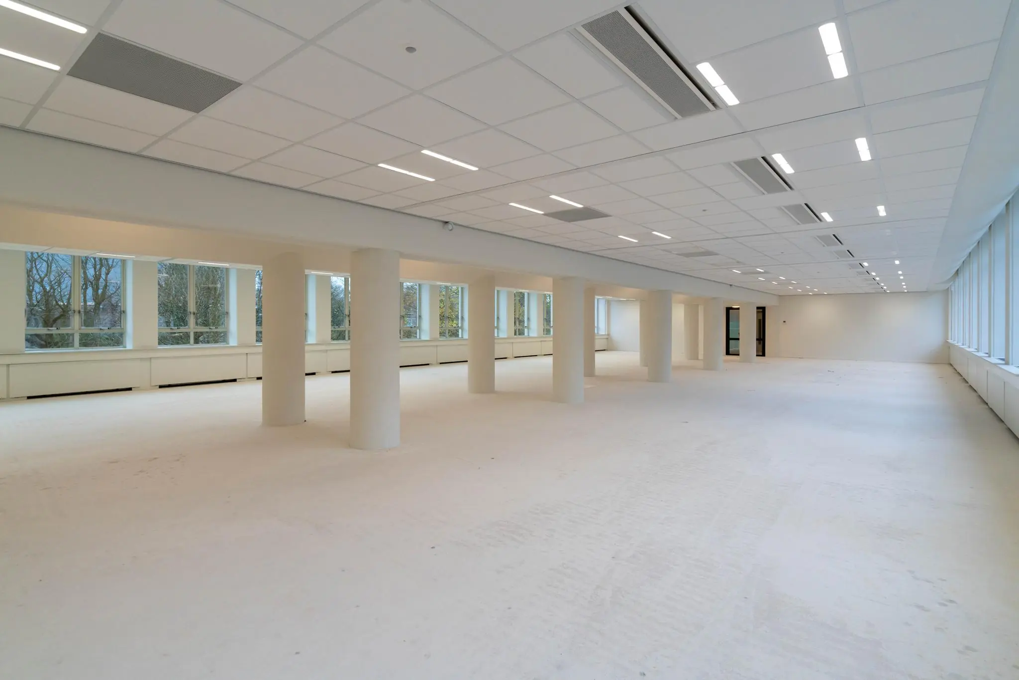 Lichte, lege kantoorruimte aan de Wassenaarseweg met grote ramen en witte pilaren.