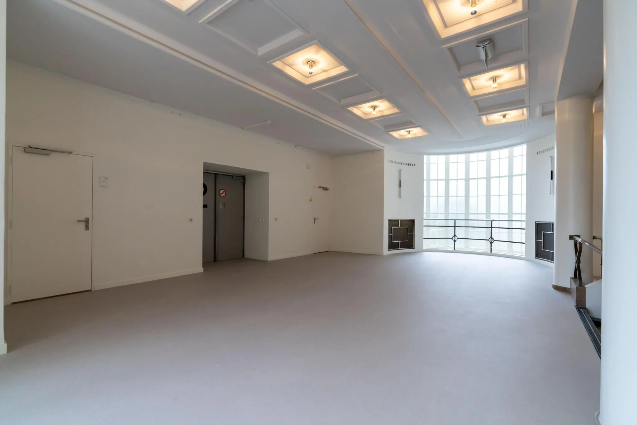 Lichte, ruime hal met liften, deuren en een grote rond raam aan de Wassenaarseweg.