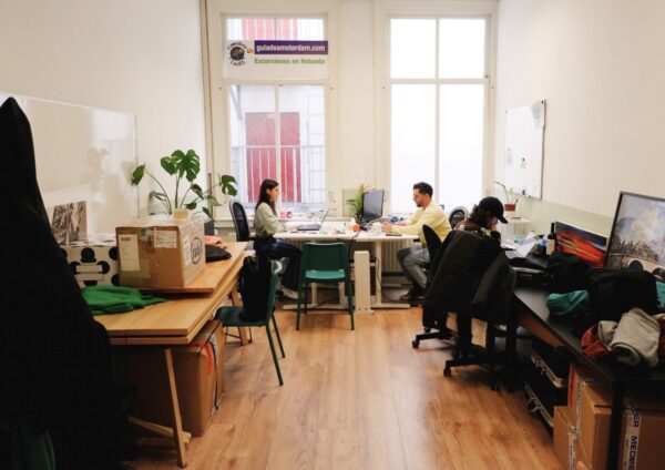 Kantoorruimte aan de Raadhuisstraat met vier mensen werkend aan bureaus bij grote ramen.