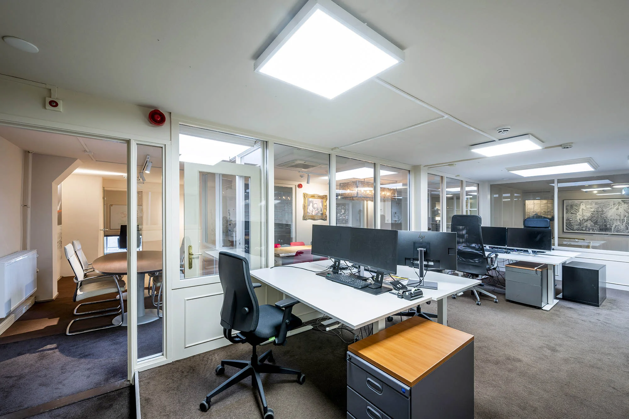 Modern kantoorinterieur aan de Herengracht met open werkplekken en een vergaderruimte achter glas.