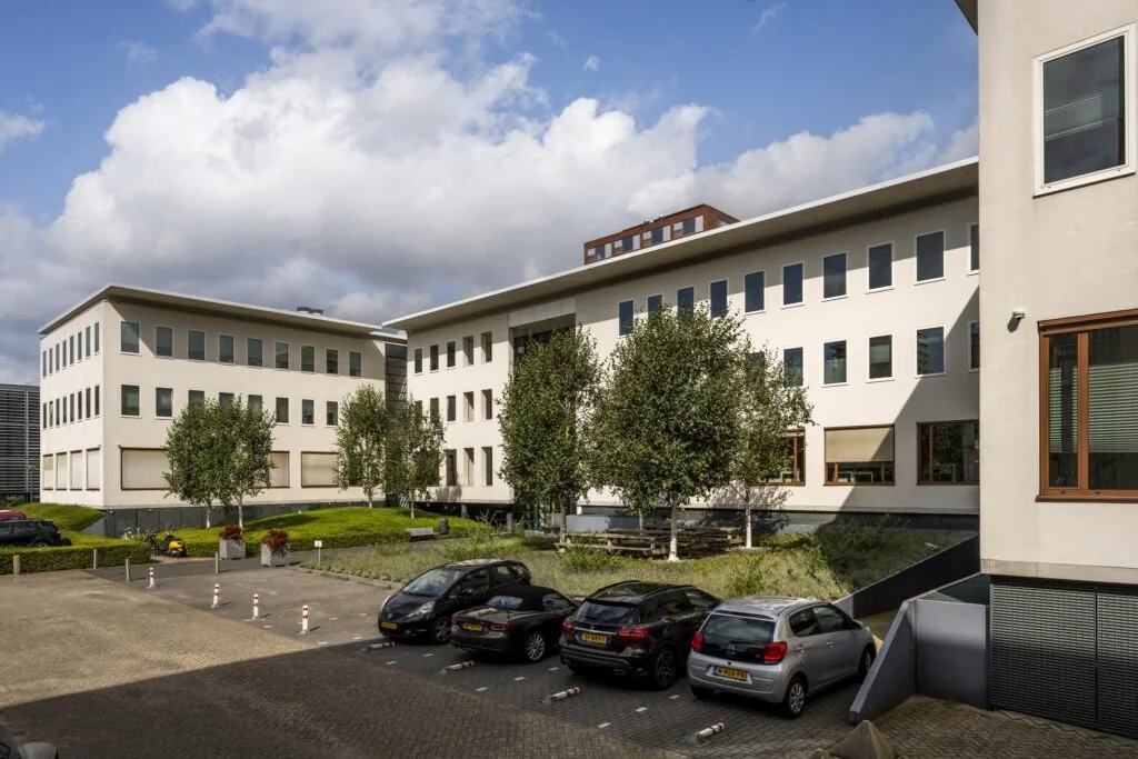 Modern kantoorgebouw aan de Naritaweg in Amsterdam met parkeerplaatsen en groenvoorziening op de voorgrond.