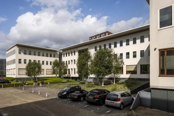 Modern kantoorgebouw aan de Naritaweg in Amsterdam met parkeerplaatsen en groenvoorziening op de voorgrond.