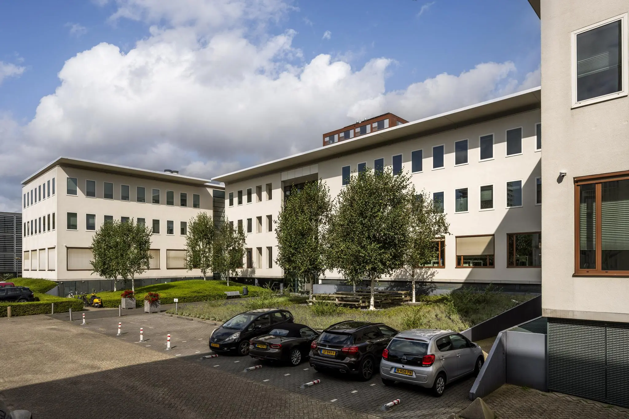 Modern kantoorgebouw aan de Naritaweg in Amsterdam met parkeerplaatsen en groenvoorziening op de voorgrond.