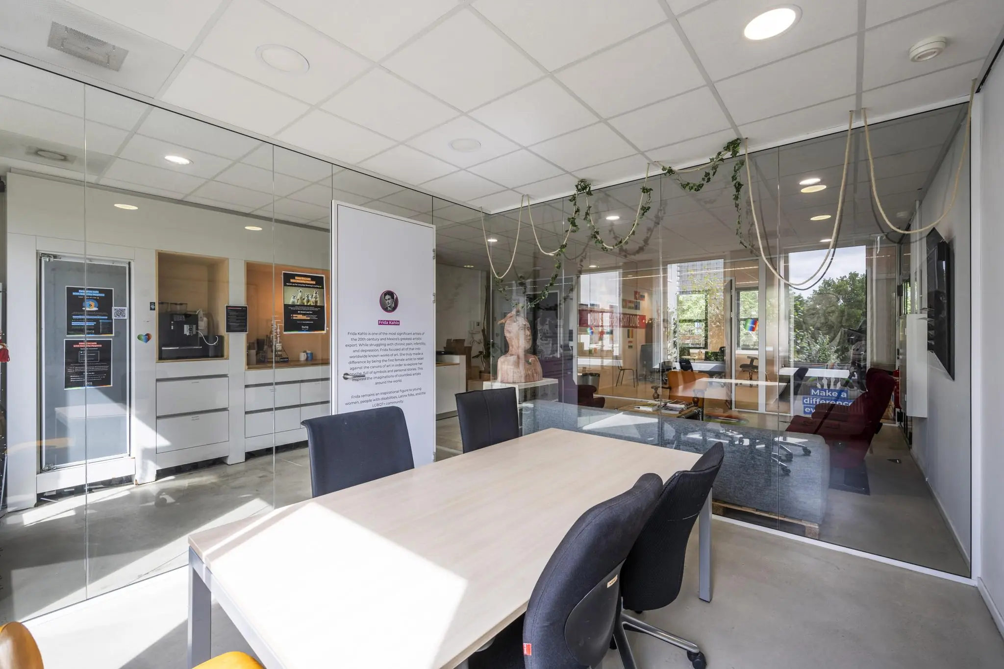 Vergaderruimte aan de Naritaweg met glazen wanden, een houten tafel, zwarte stoelen en zicht op een gemeenschappelijke kantoorruimte.