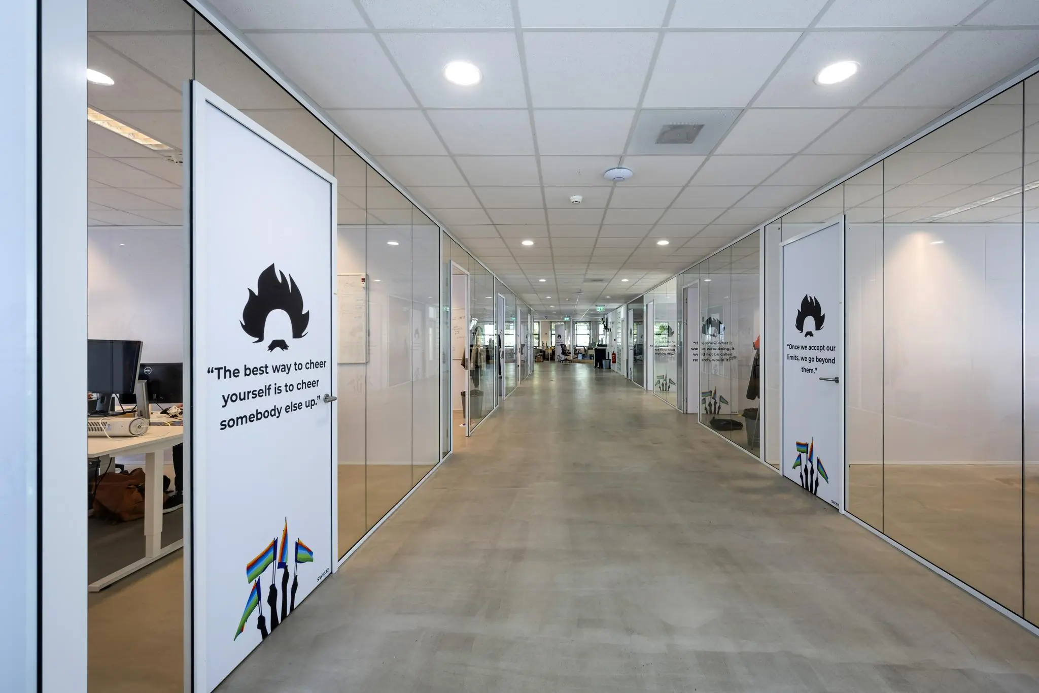 Lichte, moderne kantoorhal aan de Naritaweg met glazen wanden, inspirerende citaten op deuren en regenboogvlaggen.