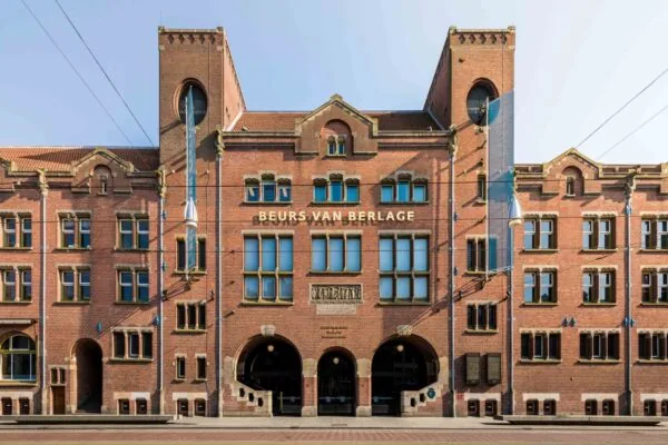 Voorgevel van de Beurs van Berlage aan het Damrak in Amsterdam, met kenmerkende rode baksteenarchitectuur en torens.