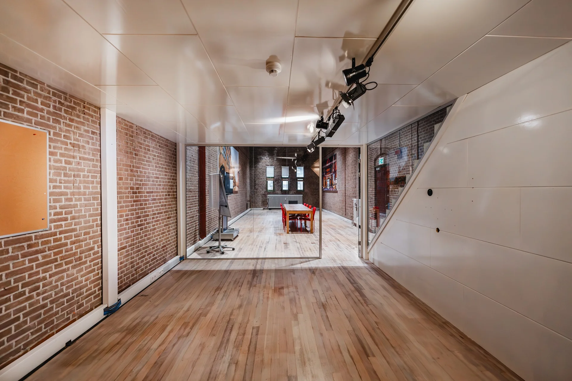 Vergaderruimte aan het Damrak met bakstenen muren, houten vloer en een glazen wand met zicht op een vergadertafel en scherm.