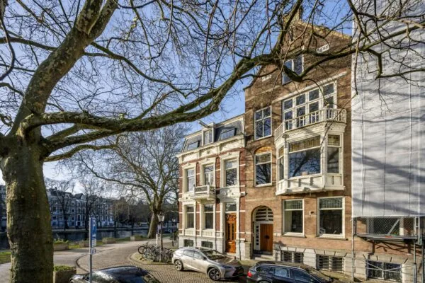 Monumentale herenhuizen aan het Eerste Weteringplantsoen in Amsterdam, omgeven door bomen en geparkeerde auto's.