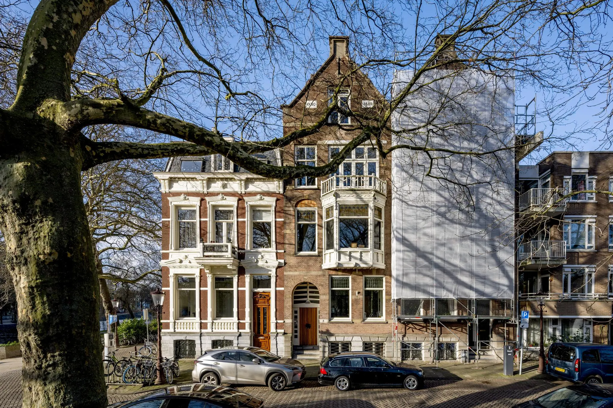 Voorgevels van historische panden aan het Eerste Weteringplantsoen in Amsterdam, met auto’s geparkeerd op de straat en een boom op de voorgrond.