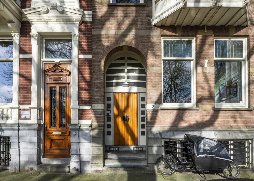Voorgevel van een woonhuis aan het Eerste Weteringplantsoen met houten deuren en een bakfiets op de stoep.
