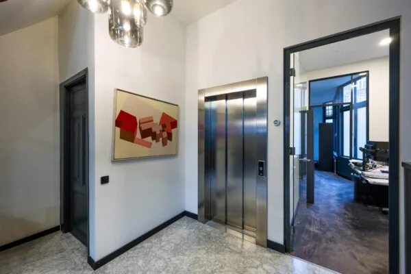 Moderne hal met een liftdeur, een abstract schilderij en een doorkijk naar een kantoorruimte in het Eerste Weteringplantsoen.