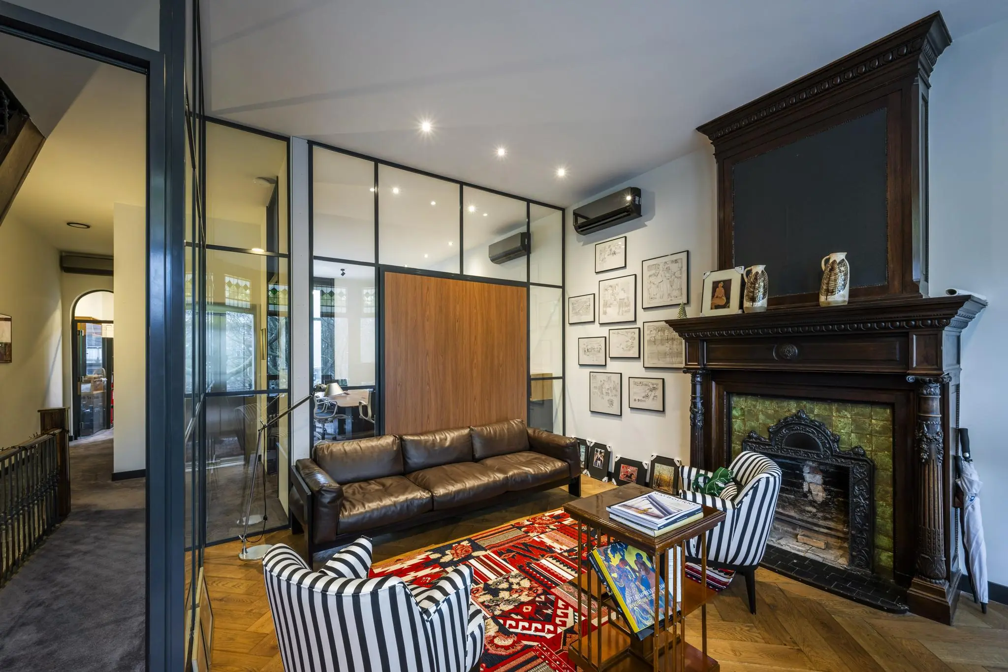 Smaakvol ingerichte zithoek in het Eerste Weteringplantsoen met een leren bank, gestreepte fauteuils, een kleurrijk vloerkleed en een klassieke open haard.