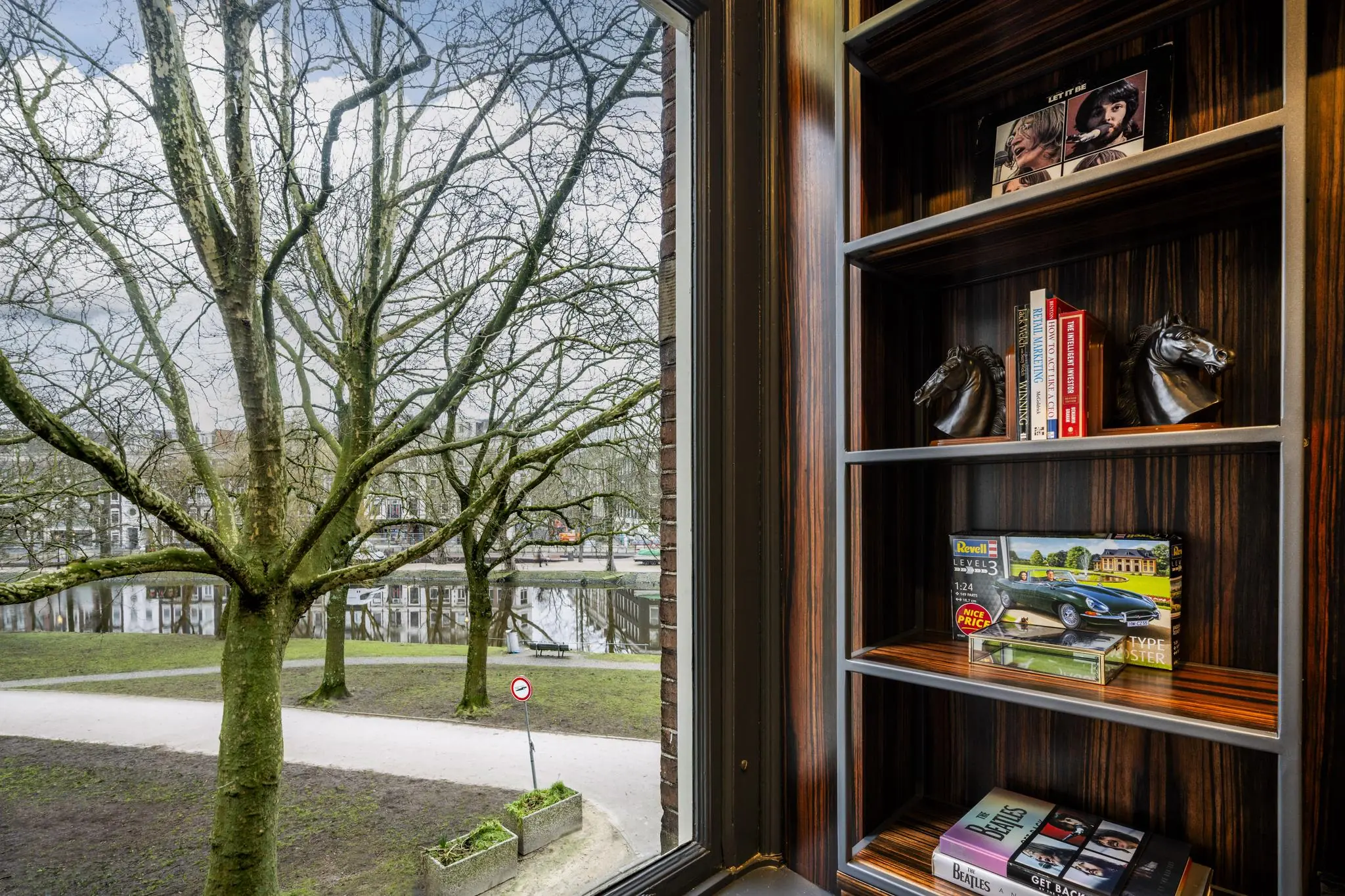 Uitzicht vanuit een raam op het Eerste Weteringplantsoen met op de voorgrond een houten boekenkast met boeken, decoraties en Beatles-items.