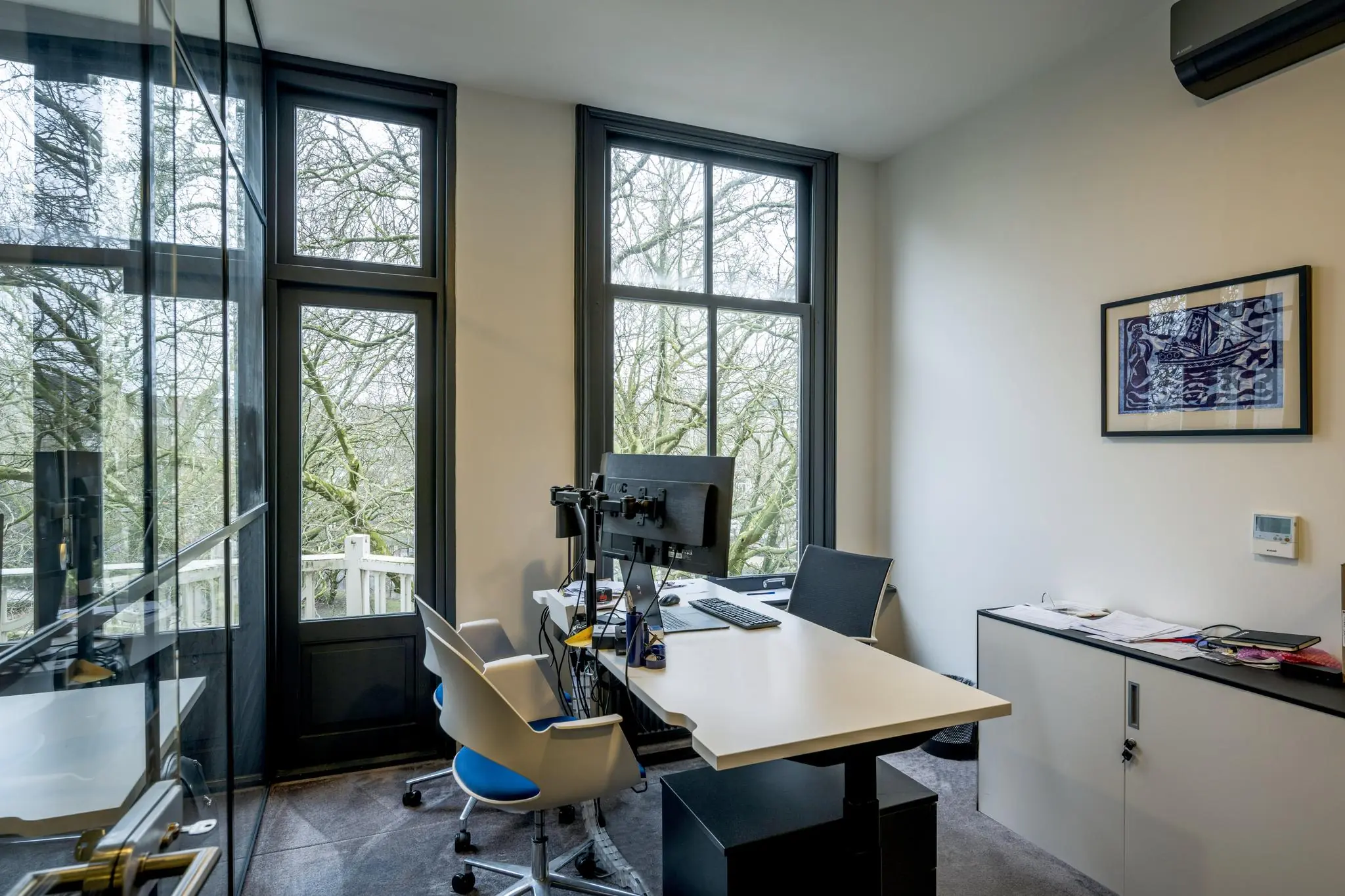Modern ingericht kantoor in het Eerste Weteringplantsoen met uitzicht op bomen door grote ramen.