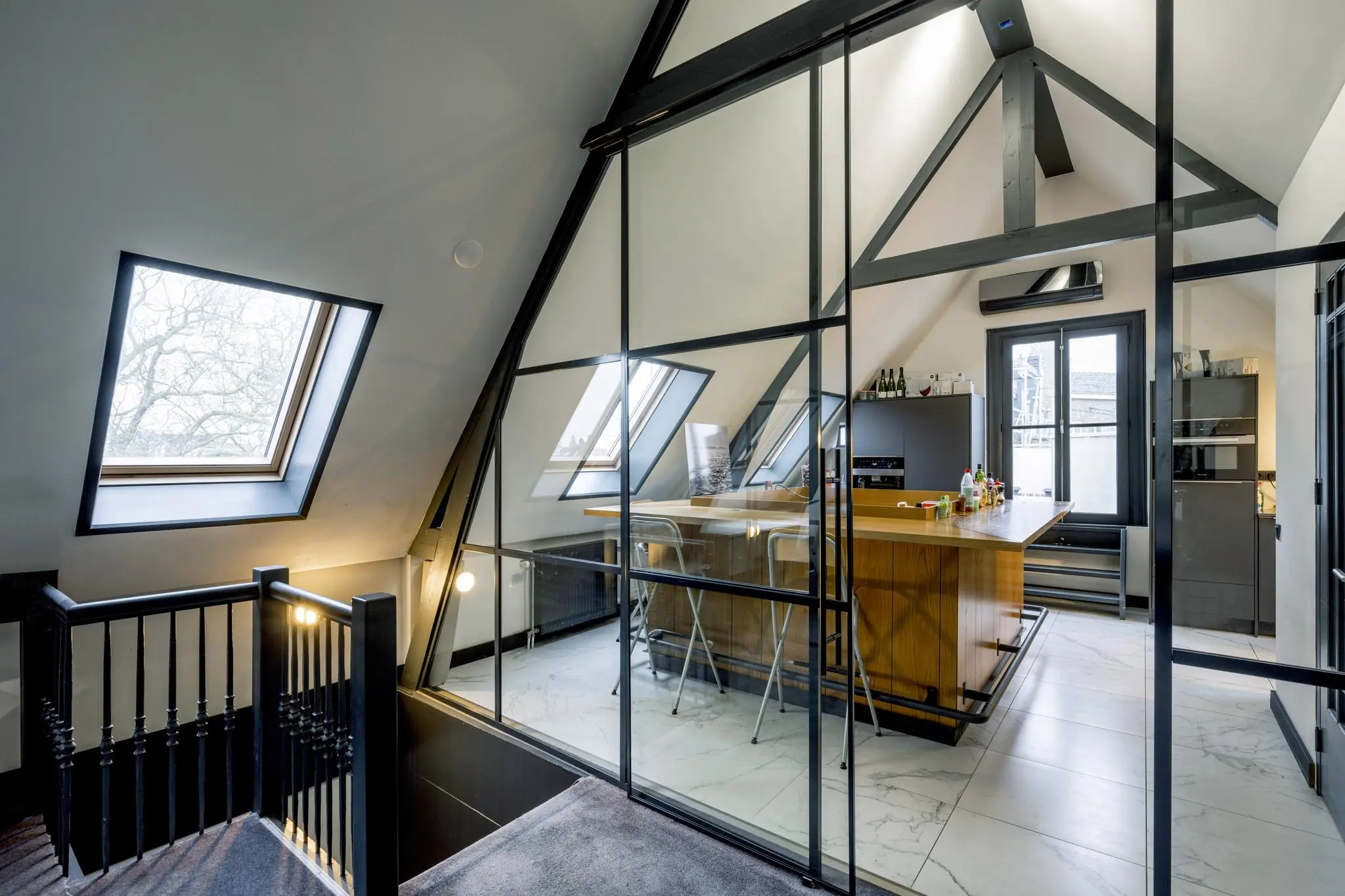 Moderne zolderruimte in het Eerste Weteringplantsoen met glazen wanden, een open keuken en schuine dakramen.