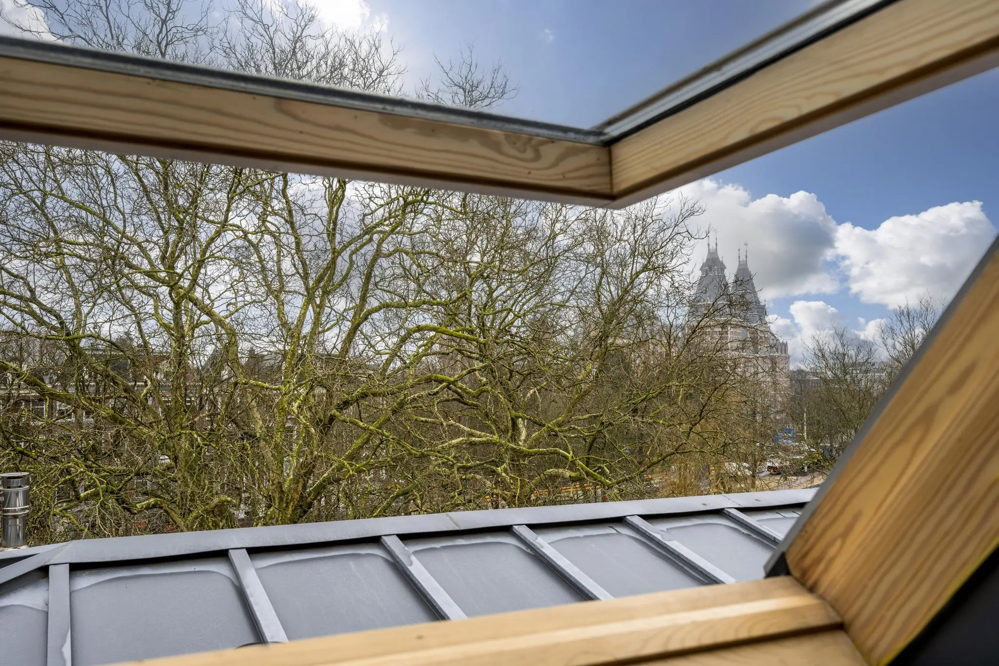Uitzicht vanuit een dakraam op het Eerste Weteringplantsoen met kale bomen en het Rijksmuseum op de achtergrond.