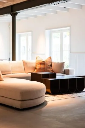 Moderne, lichte woonkamer aan de Keizersgracht met een beige hoekbank, donkerhouten salontafels en grote ramen.