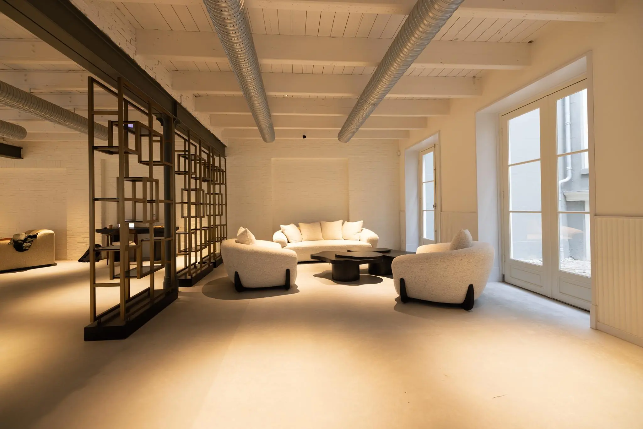 Moderne, sfeervol ingerichte lounge in een pand aan de Keizersgracht met zachte zitmeubels, houten plafond en industriële ventilatiebuizen.