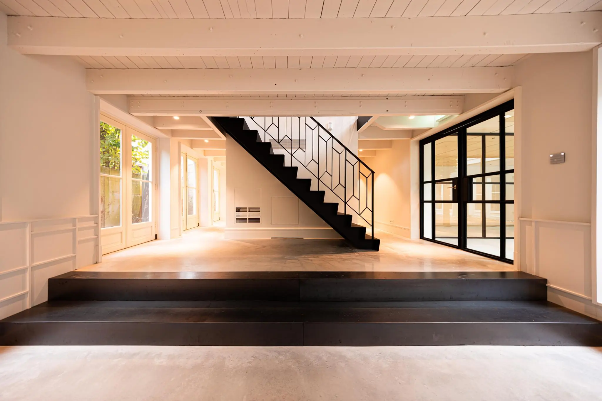 Moderne, lichte interieurruimte aan de Keizersgracht met een zwarte stalen trap en glazen deuren.