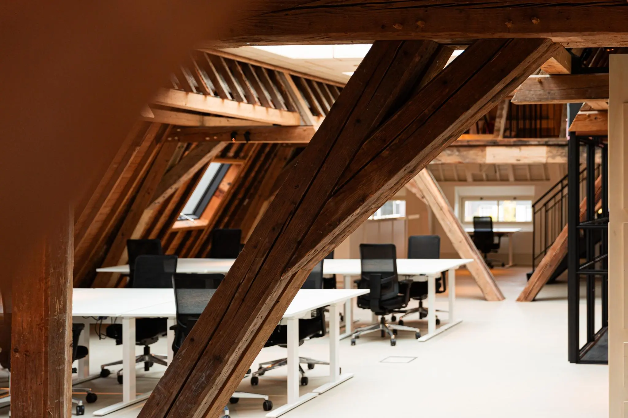Modern kantoor in een gerenoveerde zolderruimte aan de Keizersgracht met houten balken en witte bureaus.