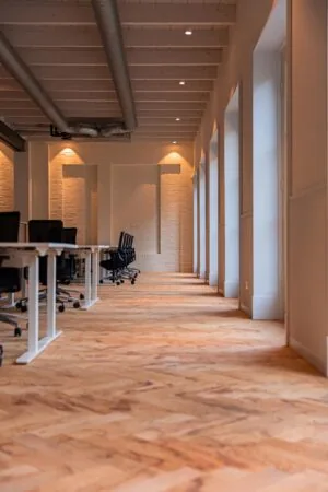 Modern kantoorinterieur aan de Keizersgracht met houten visgraatvloer, bureaus en bureaustoelen langs grote ramen.