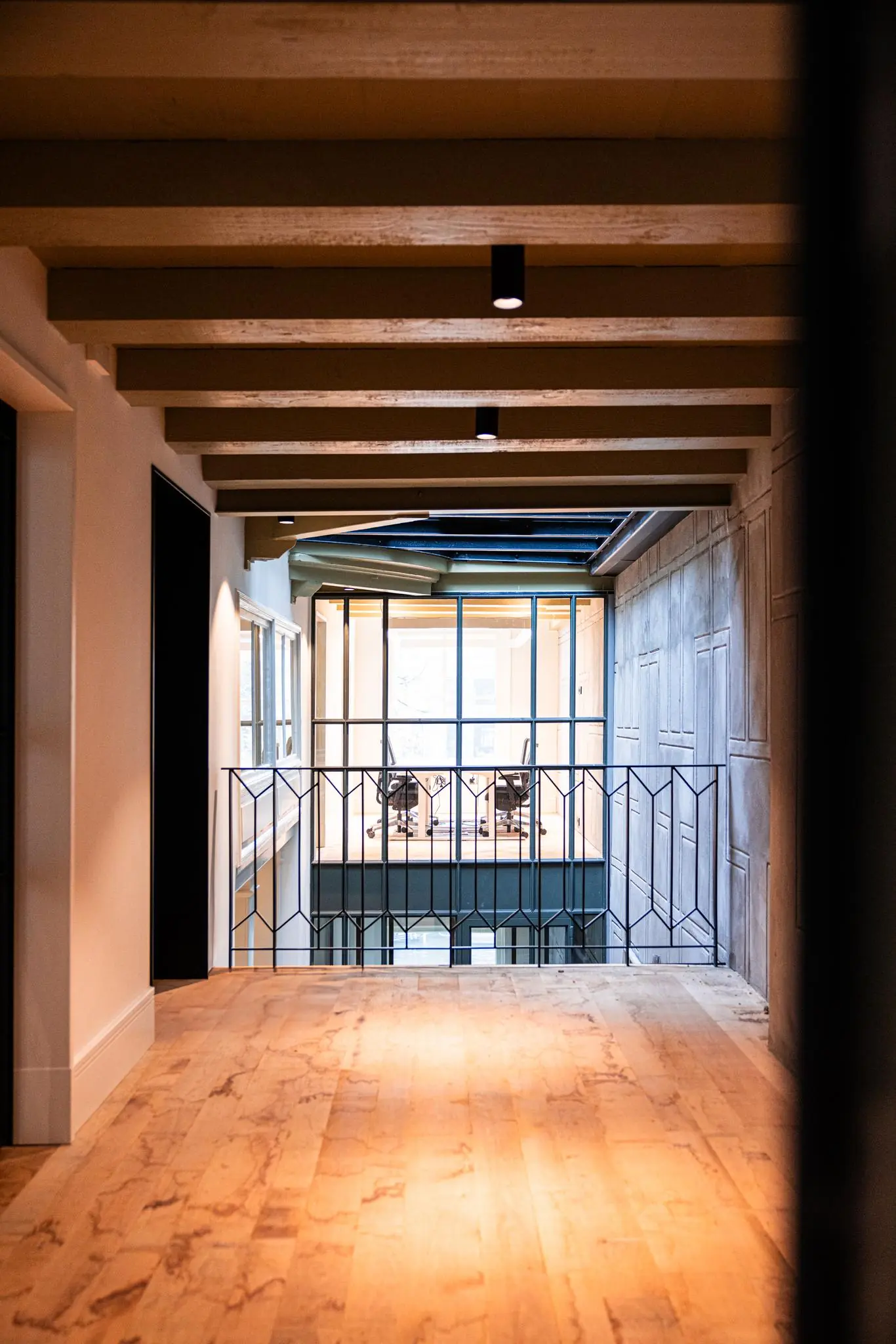 Gang met houten vloer en zicht op een glazen kantoorruimte aan de Keizersgracht met twee bureaustoelen.