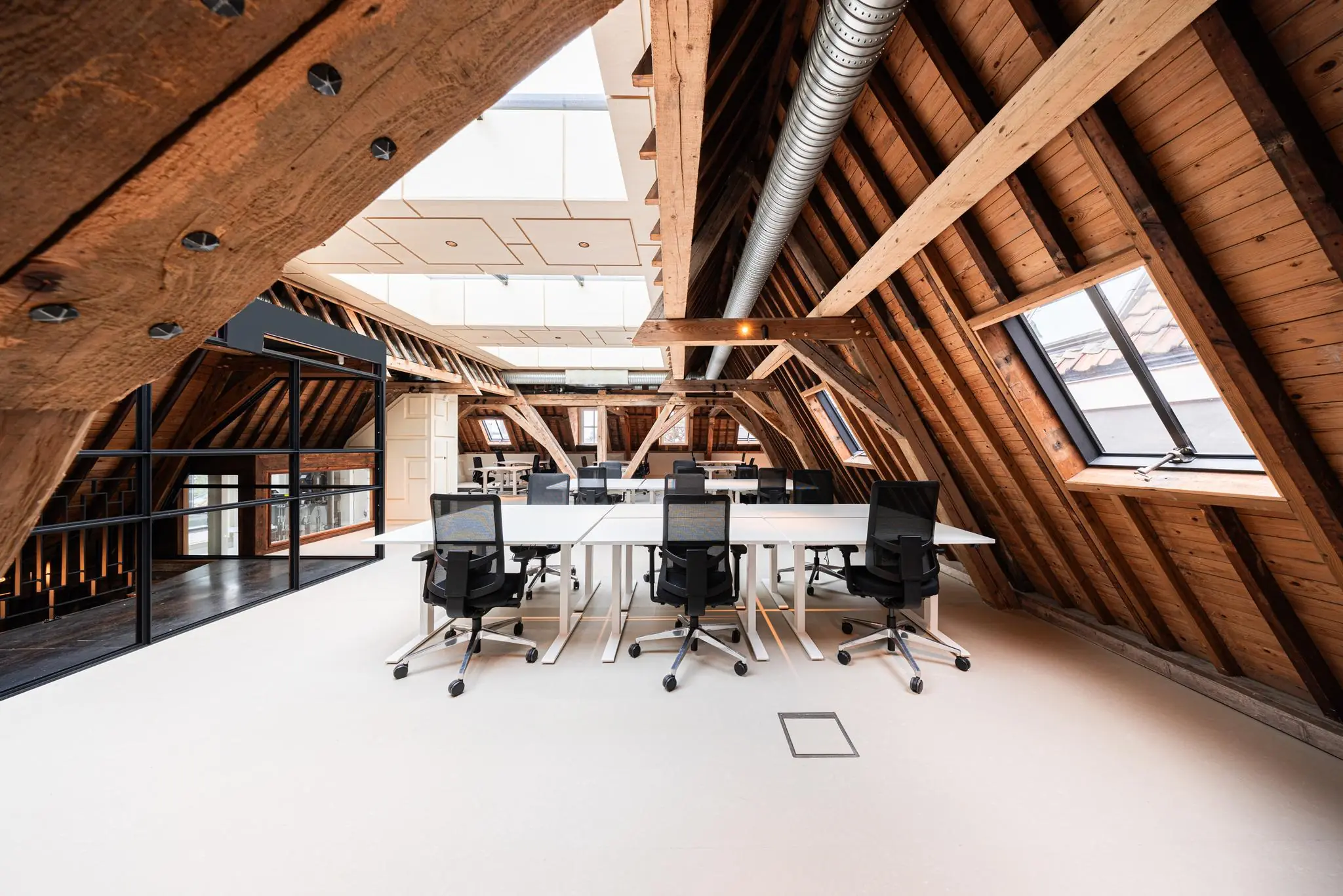 Modern kantoor in een gerenoveerde zolderruimte aan de Keizersgracht met houten balken, bureaus en bureaustoelen.