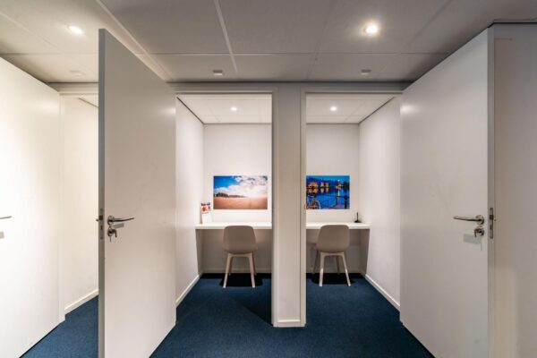 Twee moderne, afgesloten werkplekken met bureaustoel en wandfoto’s aan de Bezuidenhoutseweg.