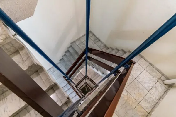 Blik naar beneden in een marmeren trappenhuis aan de Bezuidenhoutseweg met blauwe en bruine leuningen.