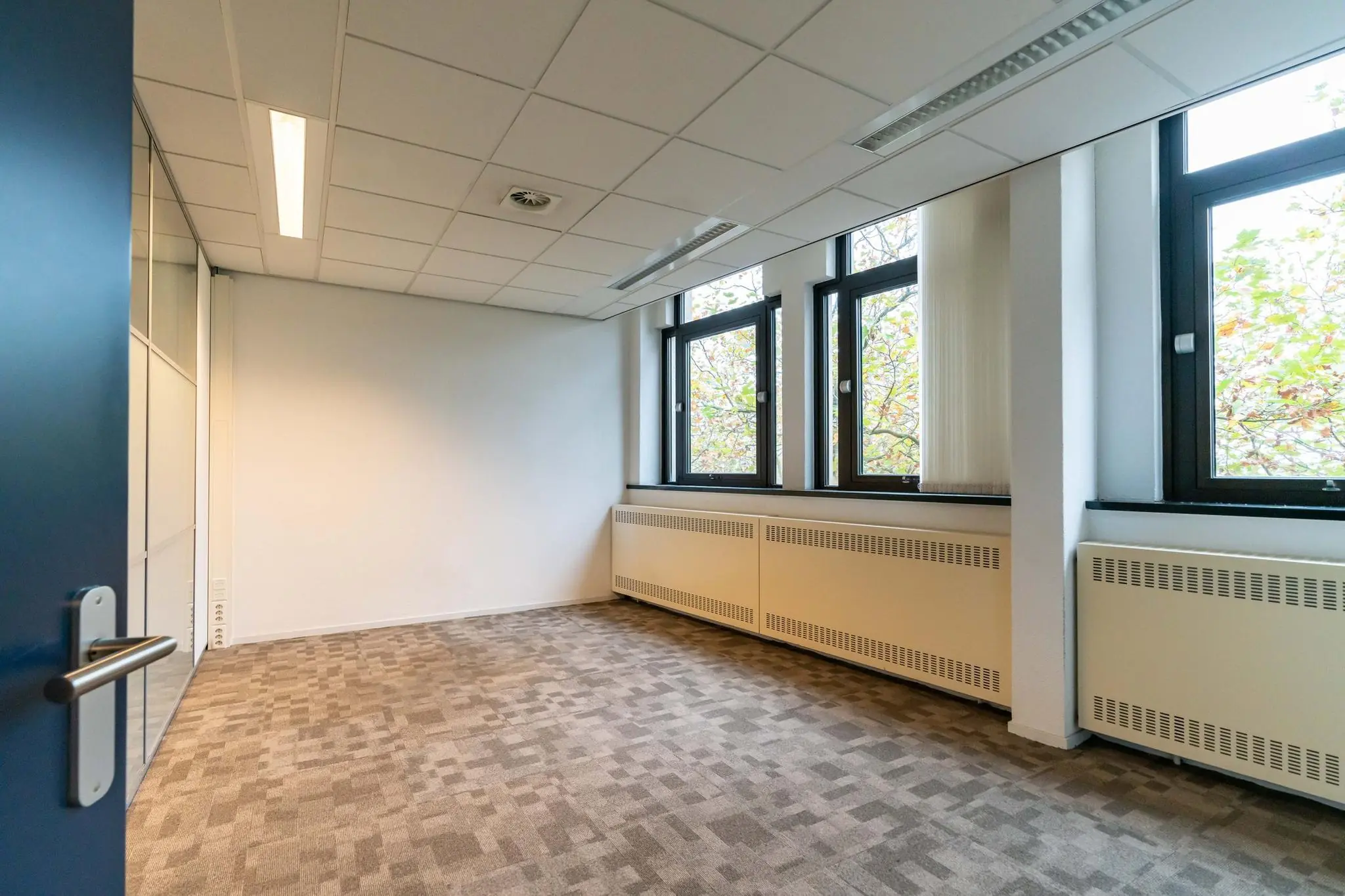 Leeg kantoorruimte met tapijtvloer en grote ramen aan de Bezuidenhoutseweg.
