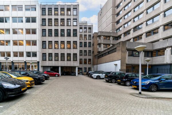 Parkeerterrein tussen kantoorgebouwen aan de Bezuidenhoutseweg met geparkeerde auto's en straatverlichting.