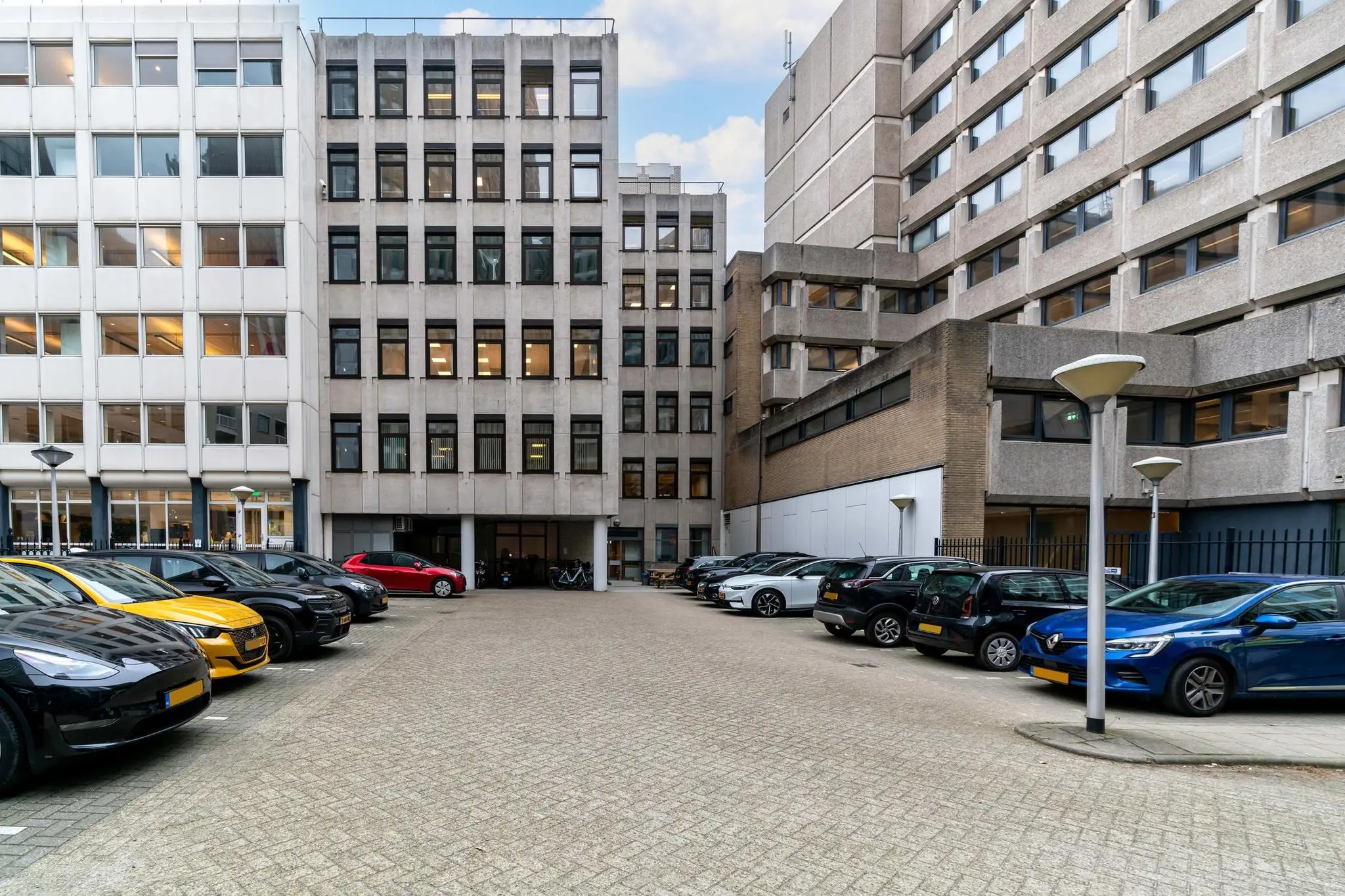 Parkeerterrein tussen kantoorgebouwen aan de Bezuidenhoutseweg met geparkeerde auto's en straatverlichting.