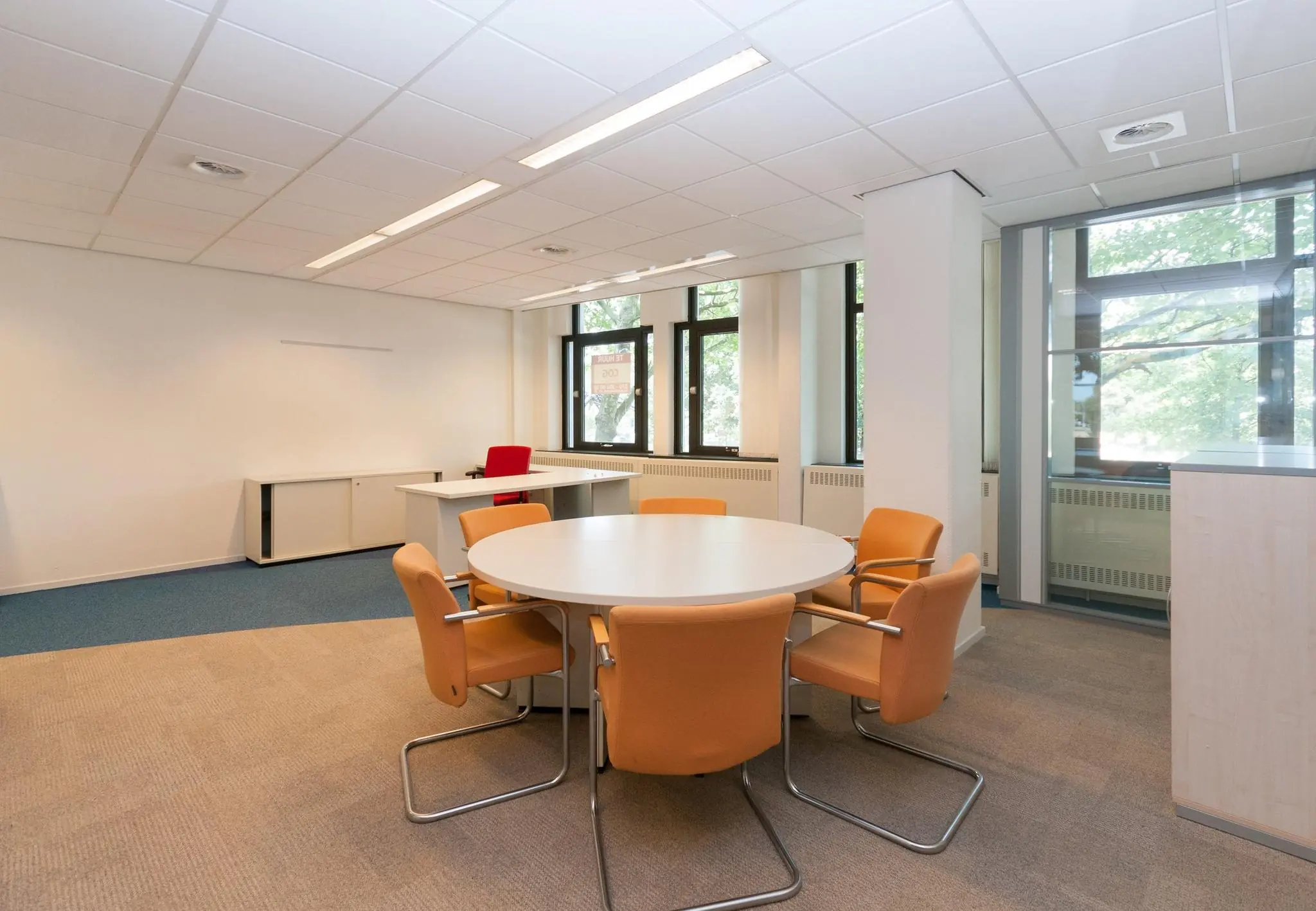 Licht en modern kantoorinterieur aan de Bezuidenhoutseweg met een ronde vergadertafel en bureau bij het raam.