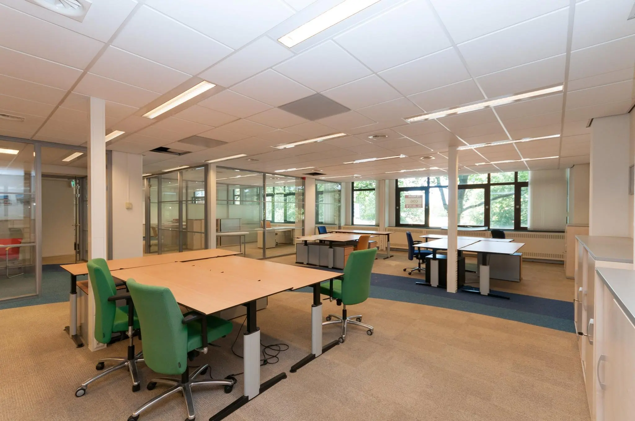 Een modern, licht kantoor op de Bezuidenhoutseweg met meerdere bureaus, bureaustoelen en glazen scheidingswanden.