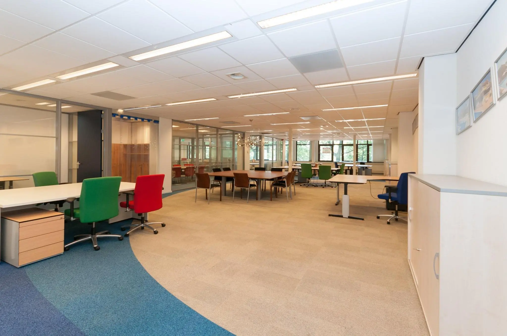 Ruim en modern kantoorinterieur aan de Bezuidenhoutseweg met diverse bureaus, kleurrijke stoelen en grote ramen.