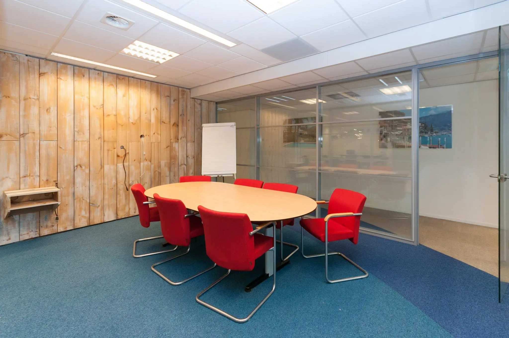 Vergaderruimte aan de Bezuidenhoutseweg met ovale tafel, zes rode stoelen, flip-over en glazen wanden.