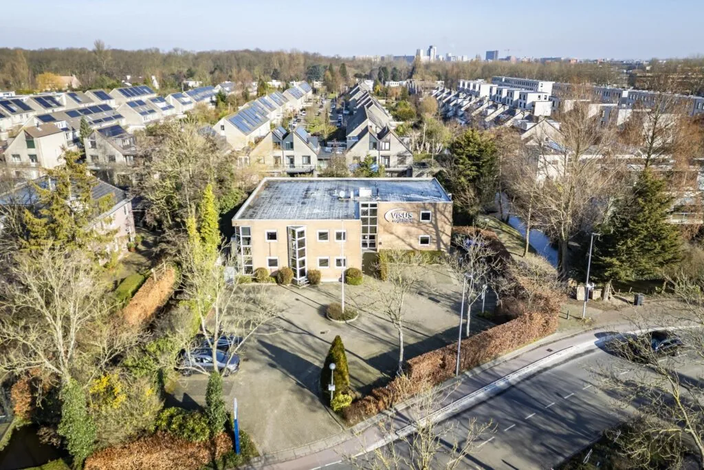 Luchtfoto van het Visus Oogkliniek-gebouw aan de 's-Gravenweg, omringd door woonwijken en bomen.