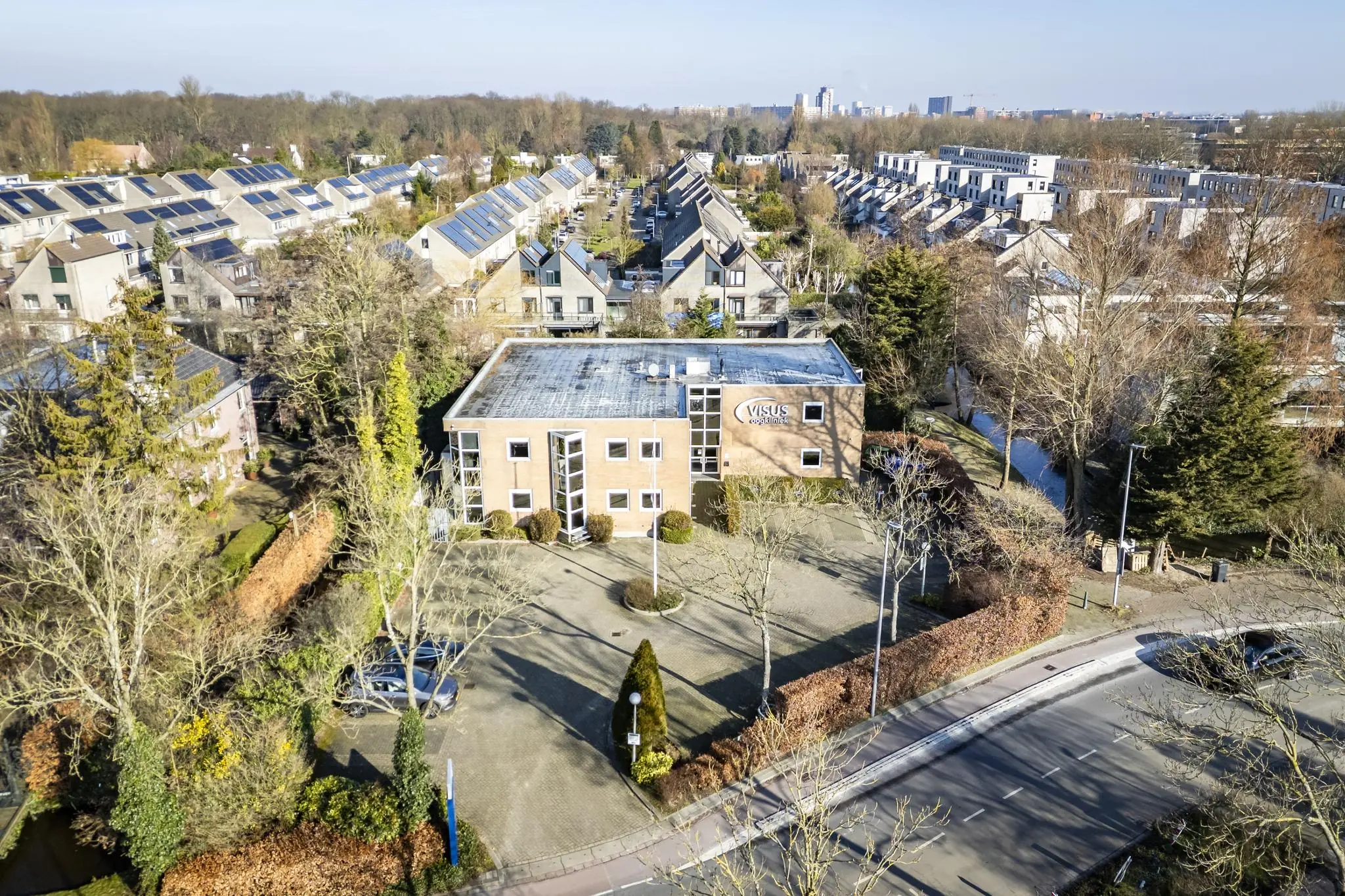Luchtfoto van het Visus Oogkliniek-gebouw aan de 's-Gravenweg, omringd door woonwijken en bomen.