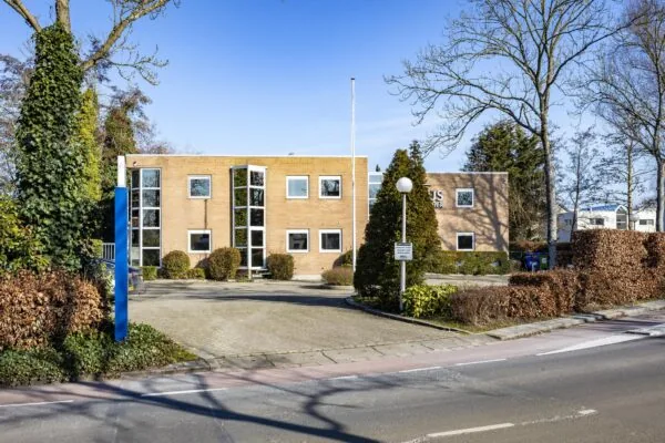 Vooraanzicht van een modern kantoorpand aan de 's-Gravenweg met een oprijlaan en omliggende bomen en struiken.