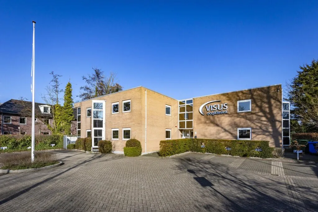 Voorgevel van het gebouw van Visus Oogkliniek aan de 's-Gravenweg, met parkeerplaatsen op de voorgrond.