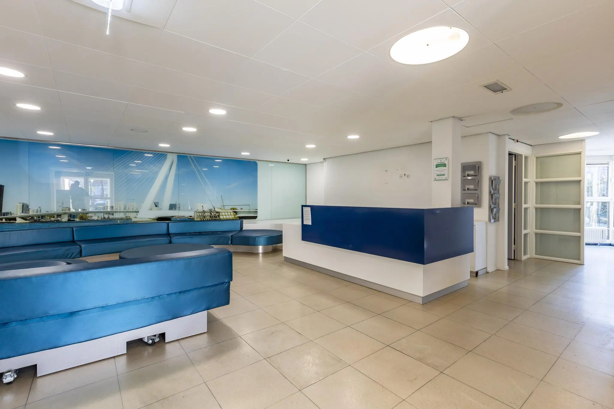 Moderne wachtruimte met blauwe zitbanken, een balie en een wanddecoratie van de Erasmusbrug.