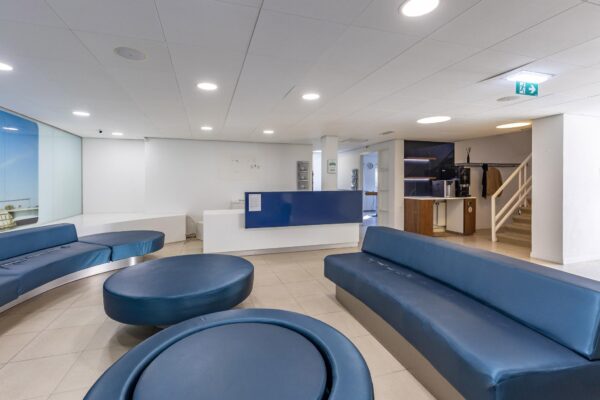 Moderne wachtruimte met blauwe zitbanken, een receptiebalie en een koffiehoek in een pand aan de 's-Gravenweg.