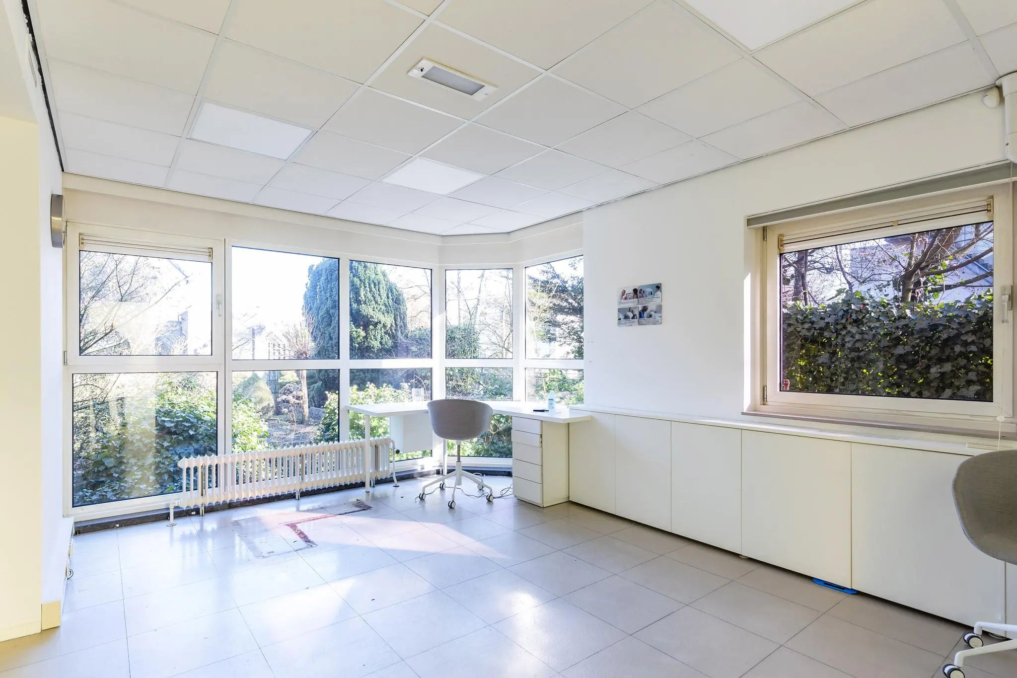 Lichte, moderne kantoorruimte aan de 's-Gravenweg met grote ramen en uitzicht op een groene tuin.